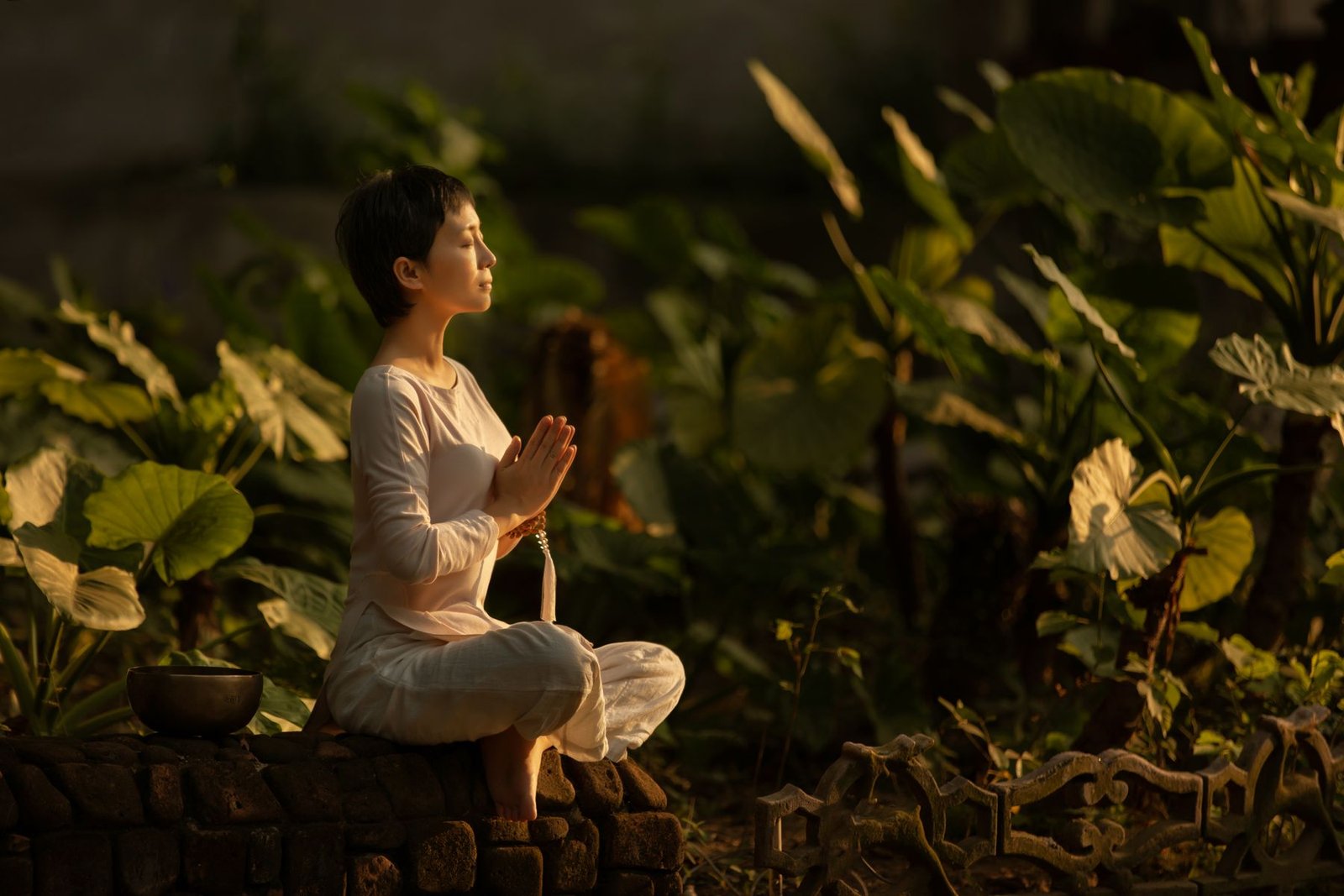 Mulher meditando em jardim ao entardecer, com sensação de bem-estar e leveza
